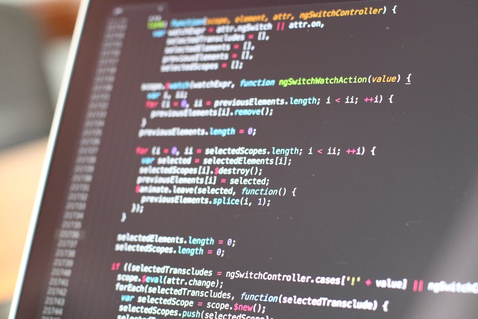 A pair of hands operating a sleek silver laptop with a dark screen displaying a code editor, suggesting a focus on programming or web development, with the background blurred to emphasize the device a